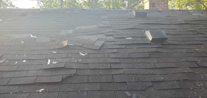 Storm-damaged roof with missing and displaced shingles