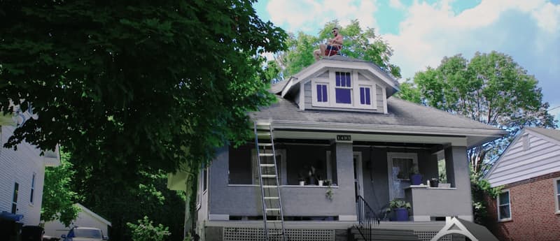 Roofer on house roof with ladder against porch